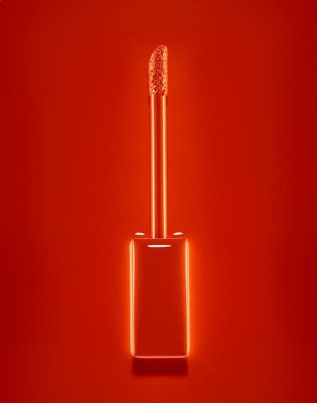 Close-up studio shot of a lipstick applicator brush on a solid red background, showing the product's texture and color.