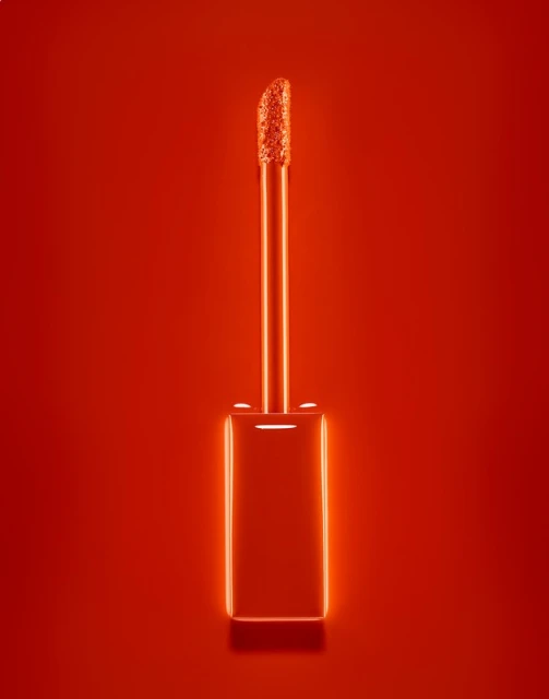 Close-up studio shot of a lipstick applicator brush on a solid red background, showing the product's texture and color.