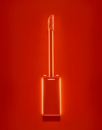 Close-up studio shot of a lipstick applicator brush on a solid red background, showing the product's texture and color.