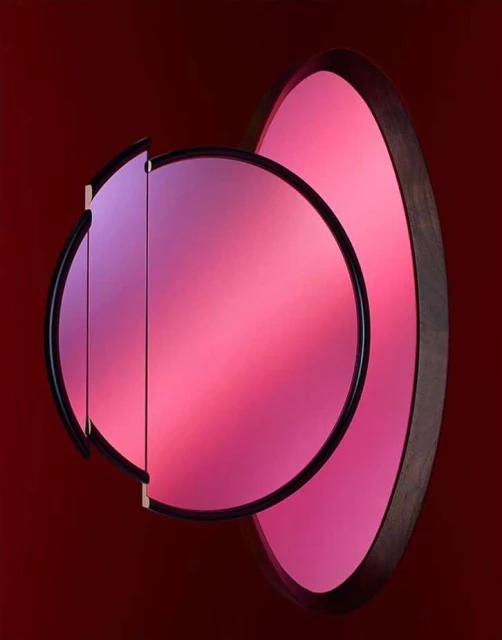 Abstract shot of pink and purple illuminated wall art featuring two overlapping geometric shapes, circular and oval, in a dark room.