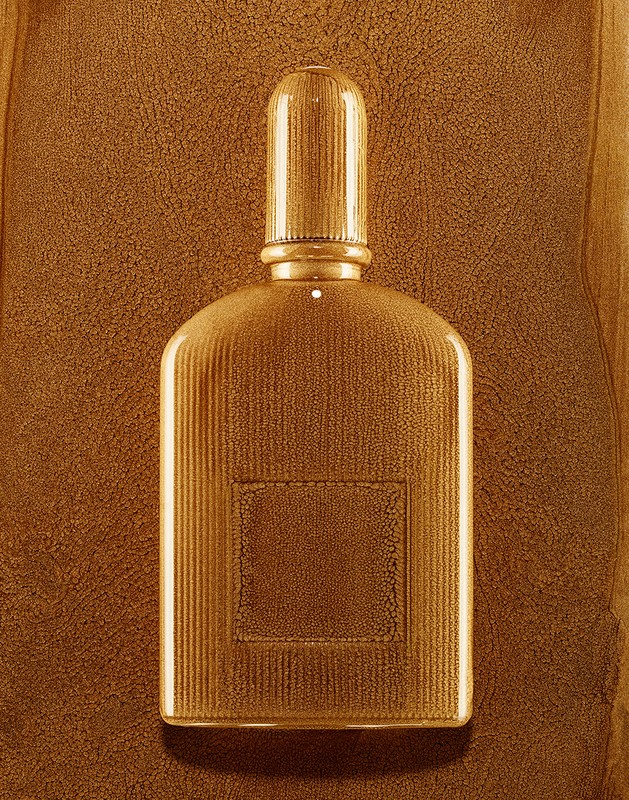 A gold ribbed perfume bottle with a matching cap photographed against a textured golden brown background by Coppi Barbieri