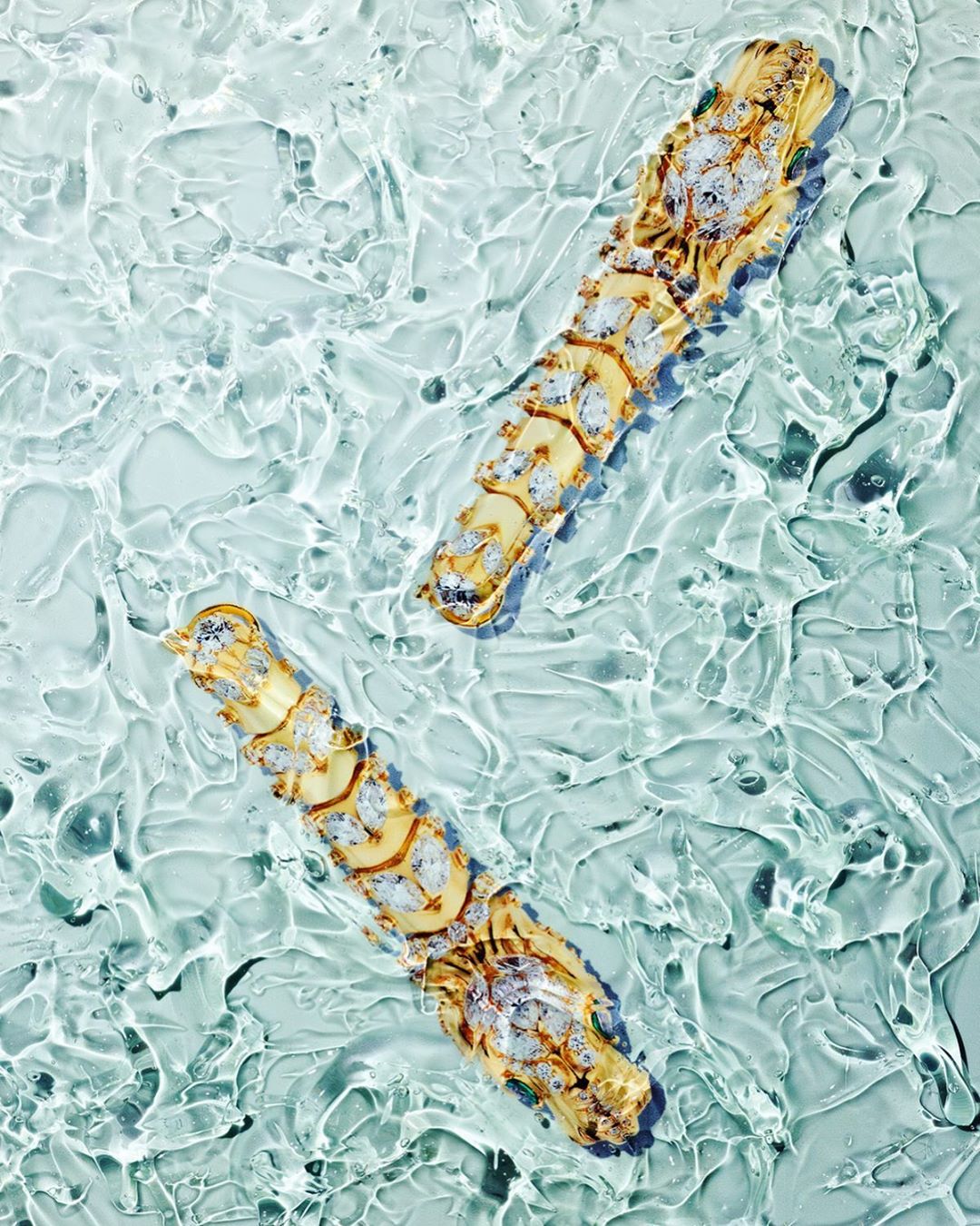 Elevated shot of two decorative gold and crystal ornaments in a rippled water setting, creating a textural and luxurious aesthetic.