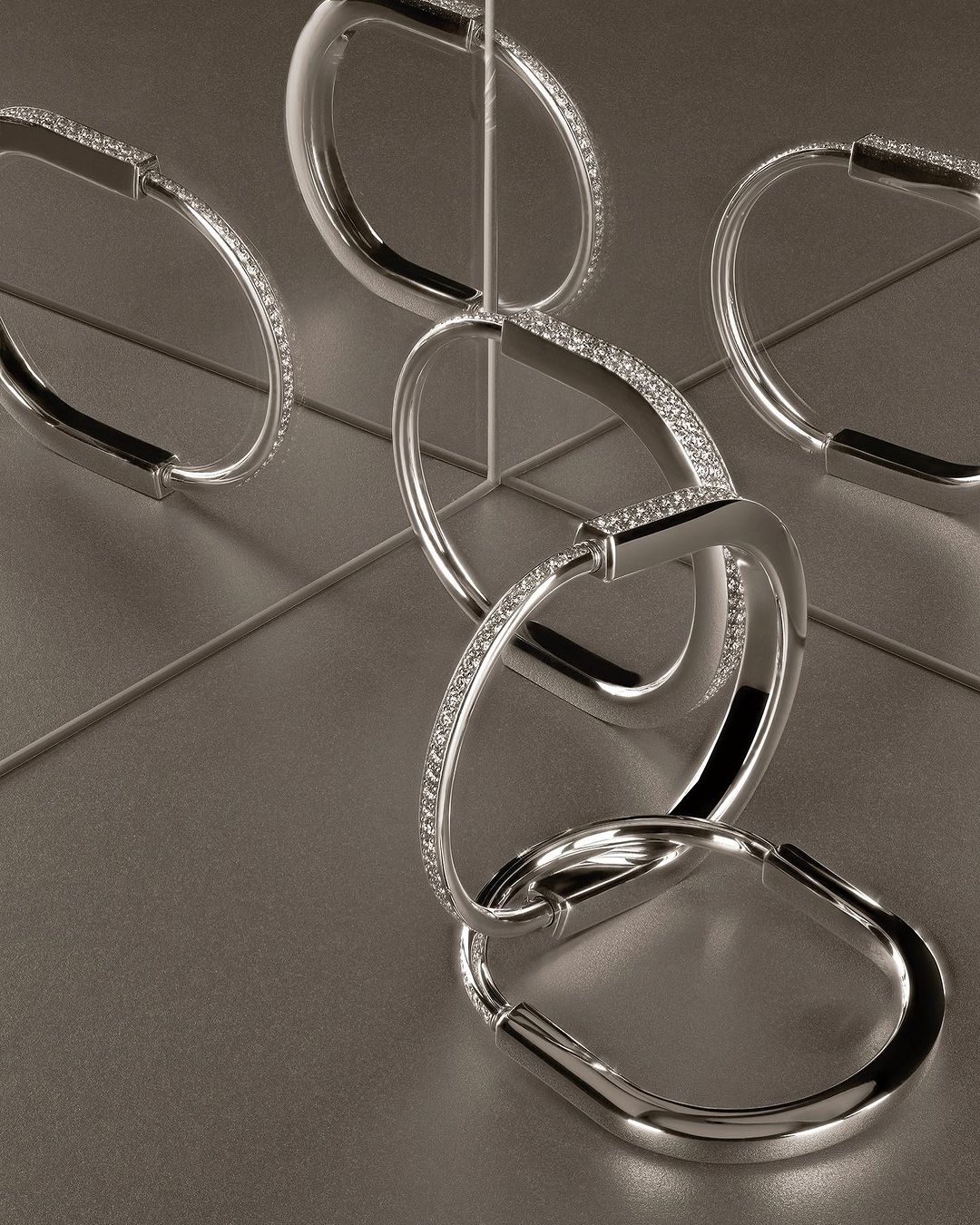 Elegant interlocking silver bracelets are arranged on a matching surface, creating a striking jewelry still life. Studio shot.
