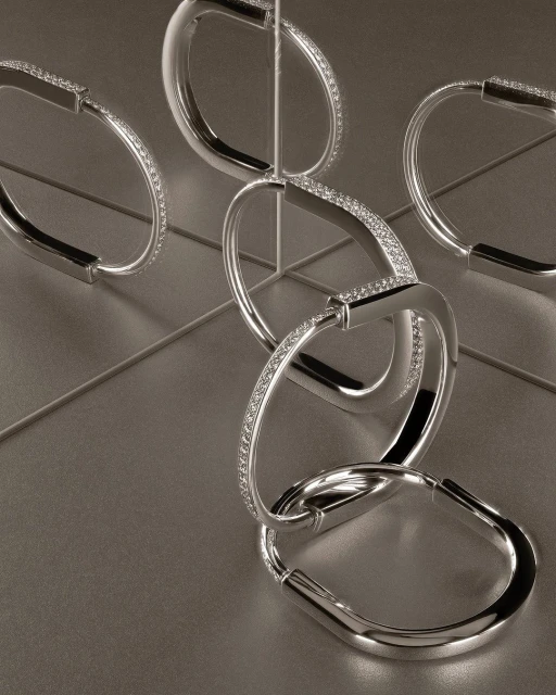 Elegant interlocking silver bracelets are arranged on a matching surface, creating a striking jewelry still life. Studio shot.