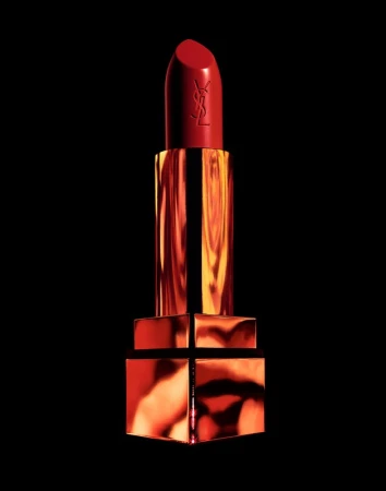 A red lipstick tube with gold metallic reflective casing against a solid black background, photographed by Coppi Barbieri.