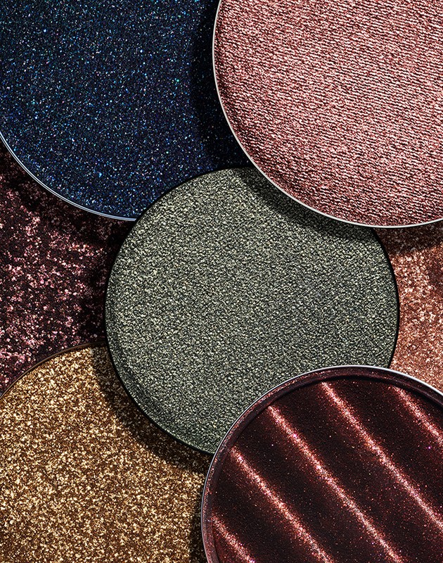 Close-up of shimmery eyeshadow palettes in blue, brown, green, pink, and copper, creating a textured, colorful display of beauty products.