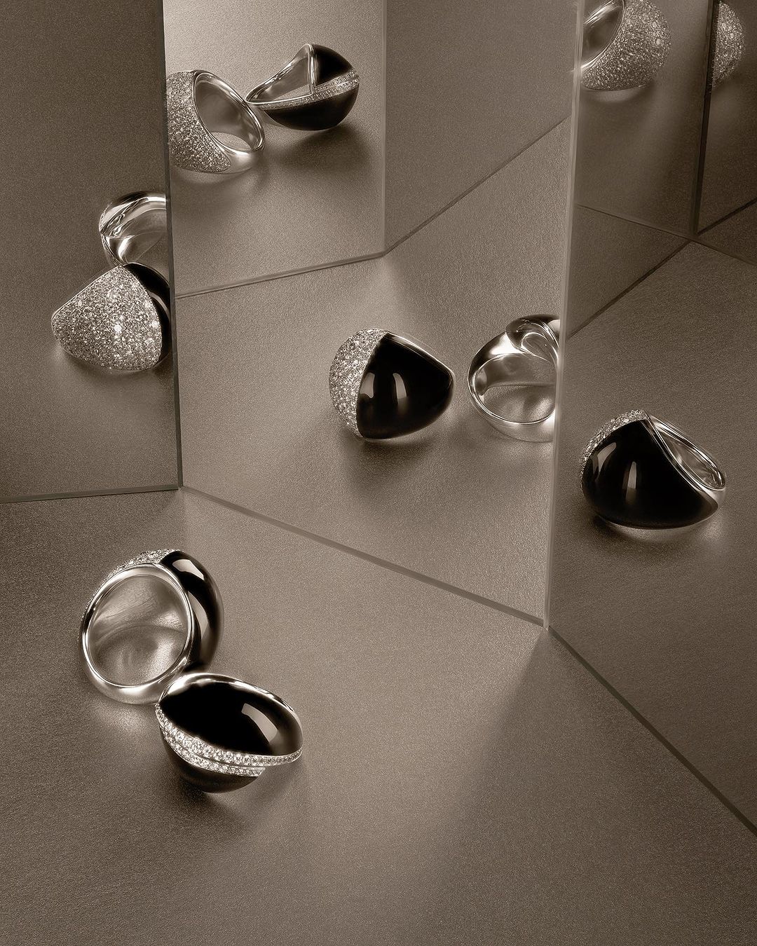 Elegant silver and black gemstone rings, set against a reflective surface, showcase contemporary jewellery design.