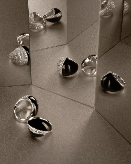 Elegant silver and black gemstone rings, set against a reflective surface, showcase contemporary jewellery design.