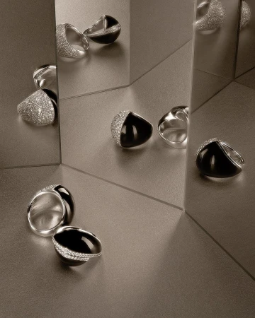 Elegant silver and black gemstone rings, set against a reflective surface, showcase contemporary jewellery design.