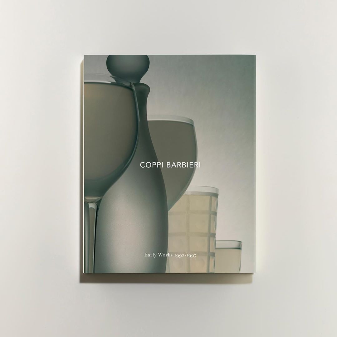 Art book cover featuring glasses in muted green and white tones, displayed against a plain white background in a studio setting.