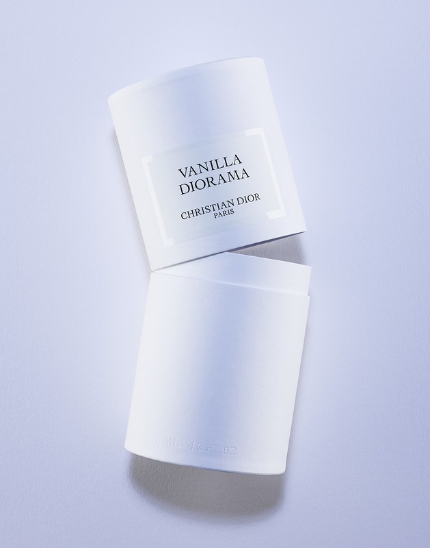 Elevated studio shot of a white Vanilla Diorama perfume container with a lid resting against it, against a white background.
