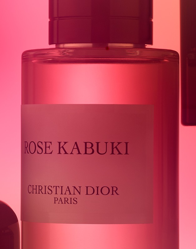 Close-up of a glass perfume bottle with a pink liquid, labeled 'Rose Kabuki' by Christian Dior, against a graduated pink background.