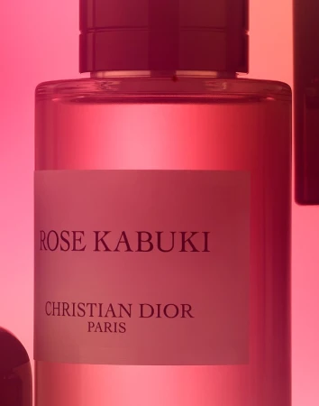 Close-up of a glass perfume bottle with a pink liquid, labeled 'Rose Kabuki' by Christian Dior, against a graduated pink background.