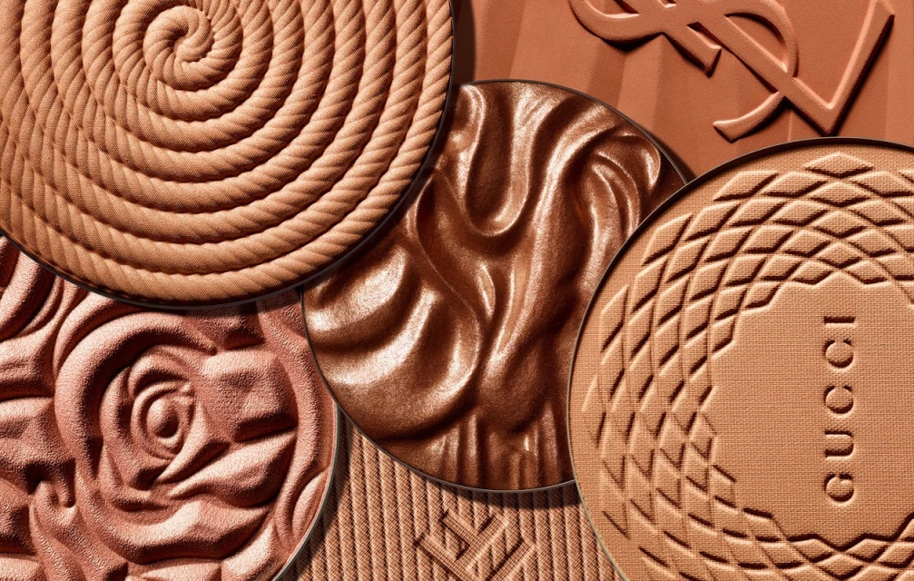Close-up of various luxury bronzer compacts from Gucci and Yves Saint Laurent featuring spiral, floral, and geometric patterns.