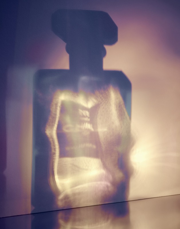 Abstract photograph of a perfume bottle with refracted light creating soft, blurred patterns on the bottle and surrounding surfaces.