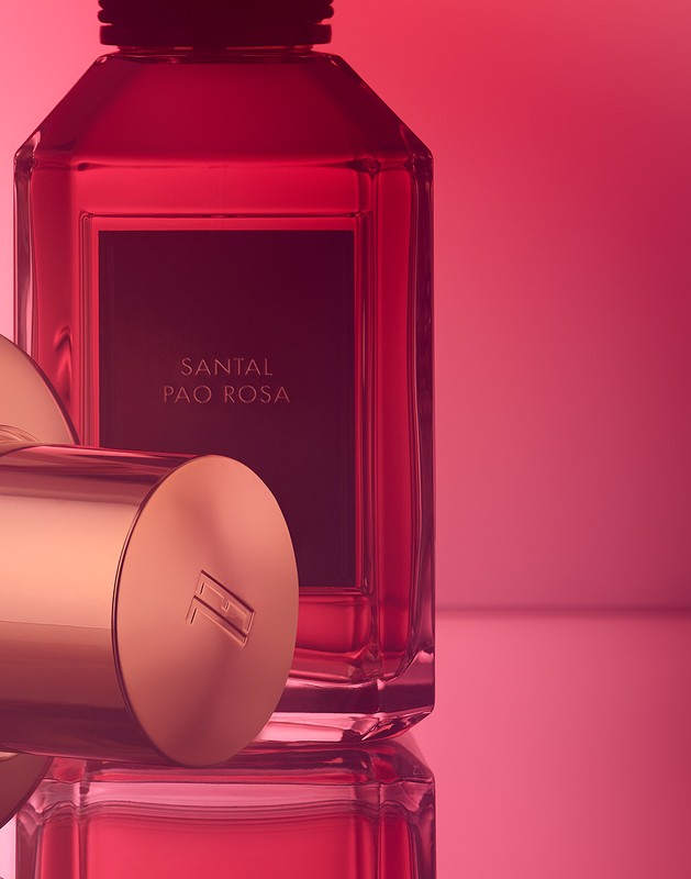 Still life shot of a pink-liquid perfume bottle and gold lid with logo against pink backdrop, capturing elegant beauty product details and color.