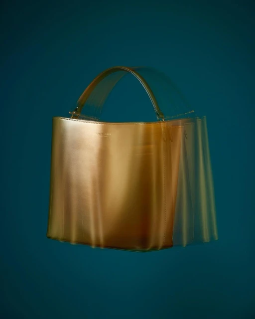Studio shot of a tan leather bucket bag with a handle, showcasing its design and material against a dark teal background.
