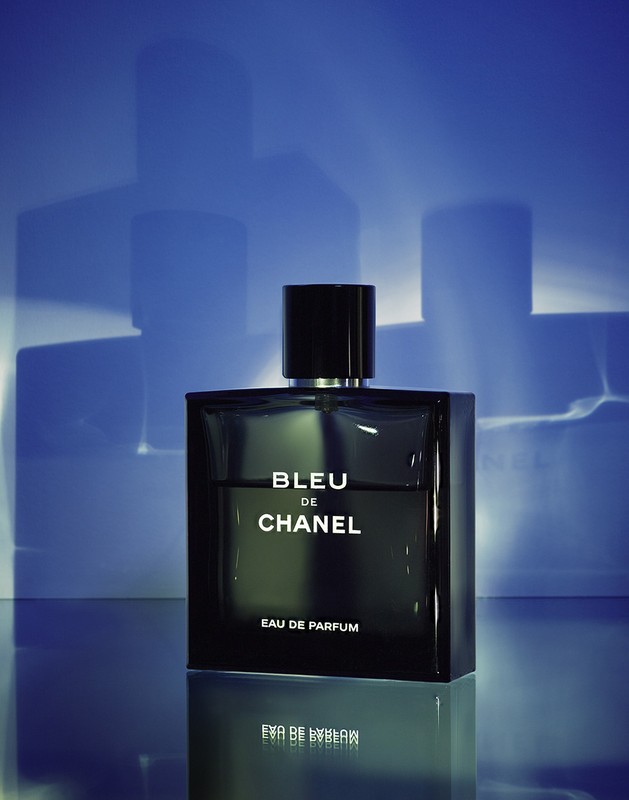 Close-up studio shot of Bleu de Chanel Eau de Parfum bottle on a reflective surface, with abstract blue lighting effects in the background.