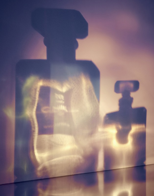 Shadows of perfume bottles on a wall create an elegant, minimalist composition with a focus on light and form, creating a visually striking effect.