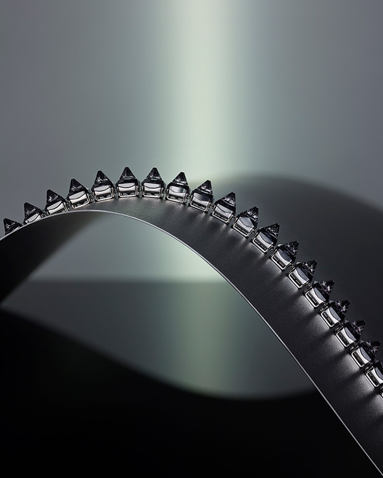 Abstract product shot featuring a curved metal surface adorned with repeating clear, triangular shapes on a graduated grey background.