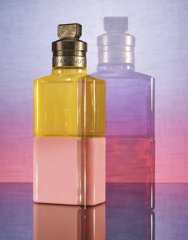 Still life studio shot of a yellow and pink perfume bottle with a second blurred purple bottle. Commercial product photography.