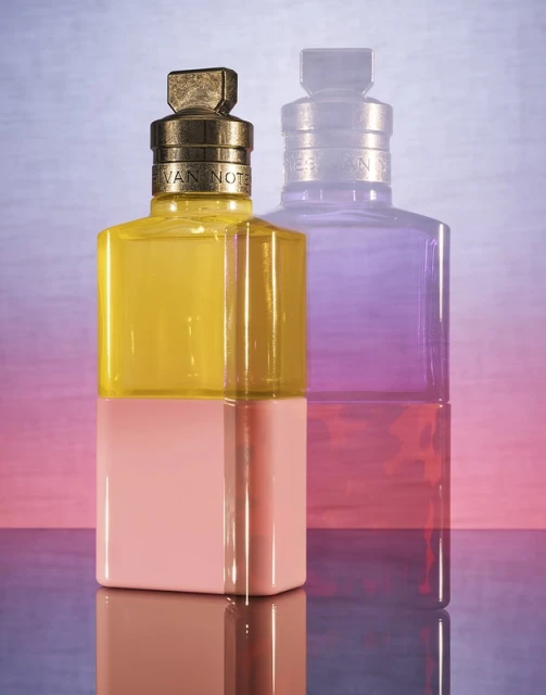 Still life studio shot of a yellow and pink perfume bottle with a second blurred purple bottle. Commercial product photography.