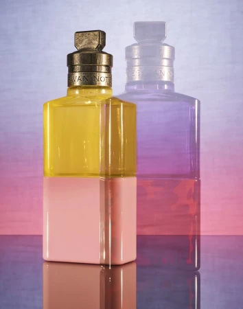 Still life studio shot of a yellow and pink perfume bottle with a second blurred purple bottle. Commercial product photography.