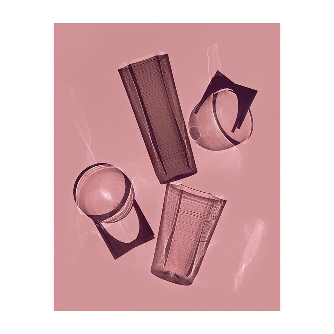 Still life shot of transparent drinking glasses in varying shapes and sizes, arranged against a pink backdrop with lens flares.