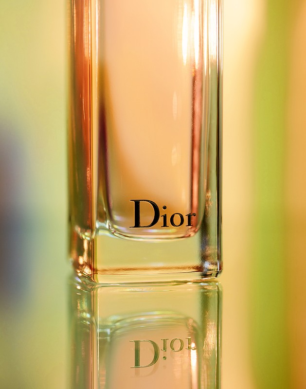Close-up shot of a Dior perfume bottle on a reflective surface with a soft, out-of-focus background showcasing the brand's logo.