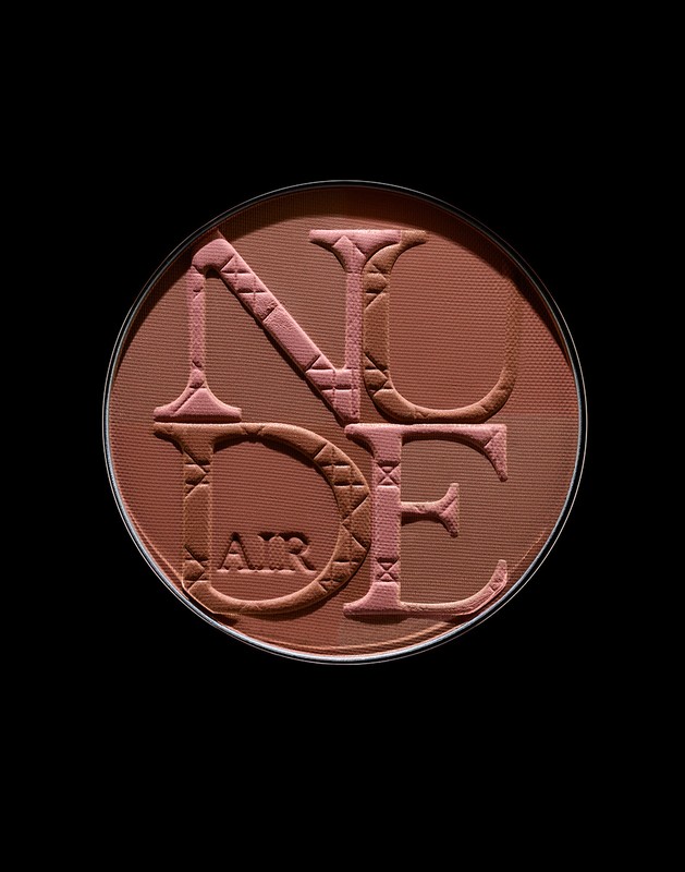 Close-up of Dior Nude Air Tan powder compact. The bronzer palette features raised lettering. Earthy tones dominate the cosmetic product.