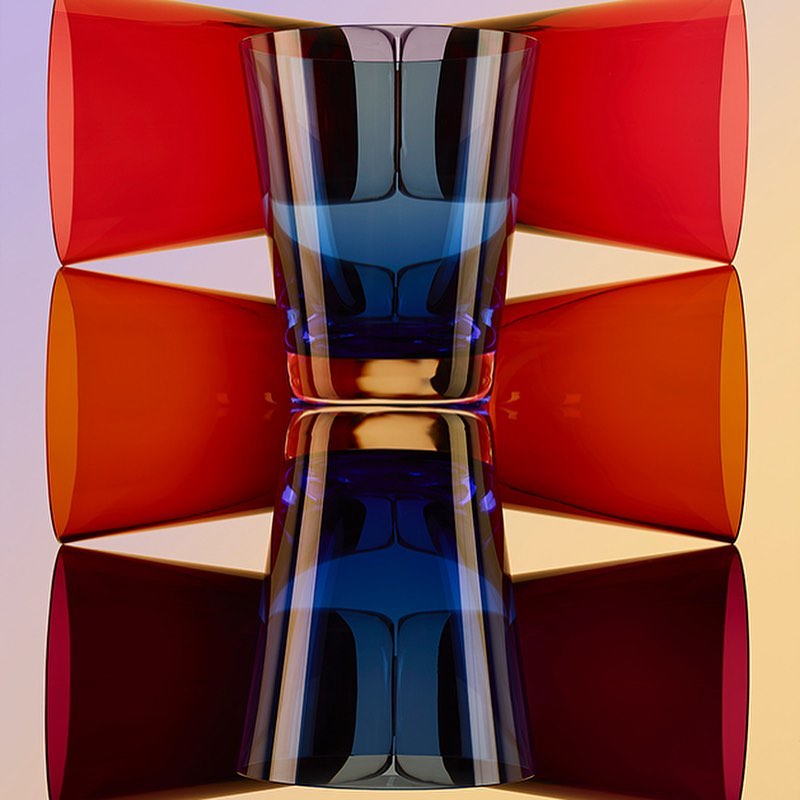 Art photography of a blue glass reflected on a surface, framed by red and orange geometric shapes, creating a symmetrical, colourful composition.
