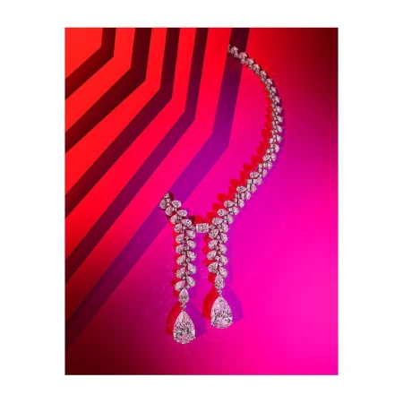 Diamond necklace with pear-shaped drops displayed against a vibrant pink and red geometric background by Coppi Barbieri.