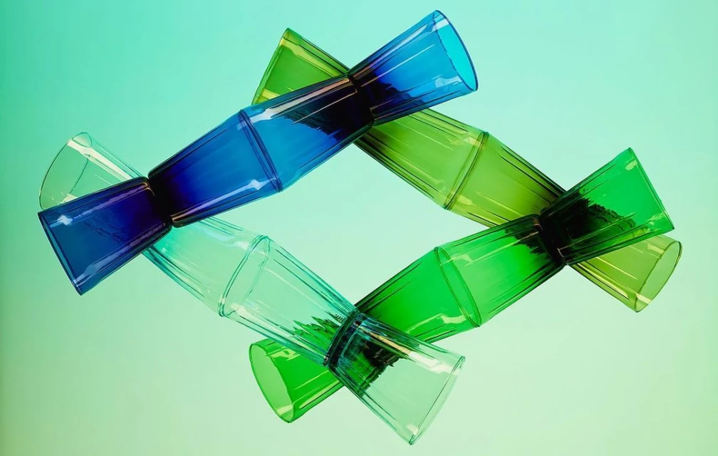 Abstract arrangement of translucent blue and green drinking glasses stacked in a diamond pattern on a light green gradient background.
