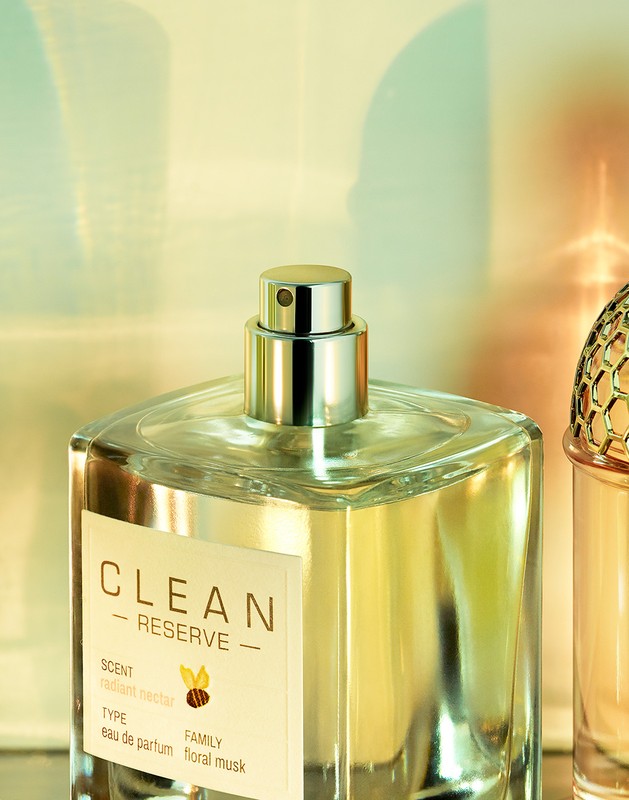 Close-up of a 'Clean Reserve' perfume bottle with a metallic nozzle, showcasing the label and golden liquid inside the transparent glass.