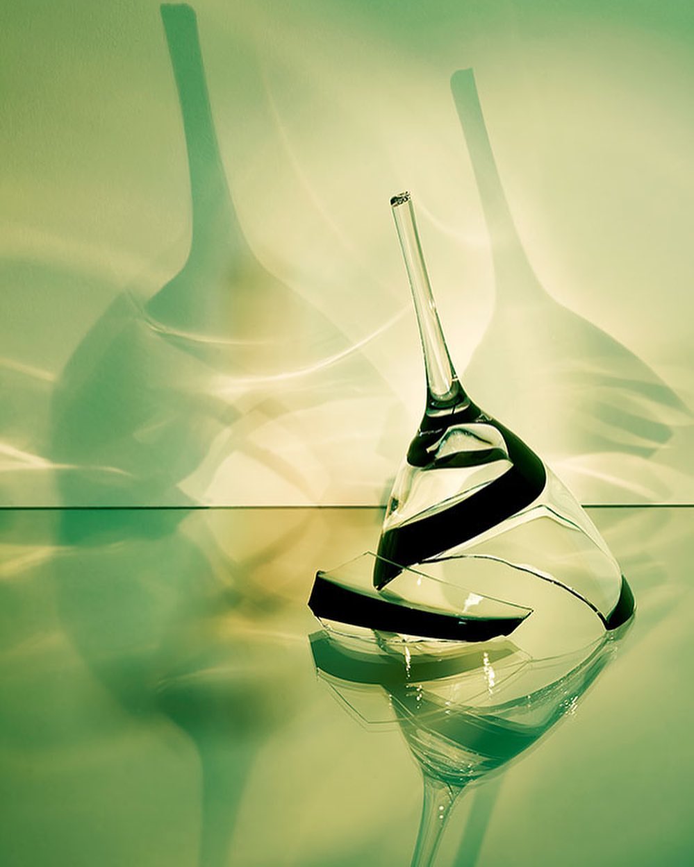 Dramatic studio shot of a broken clear glass with dark accents lying on its side and casting shadows, suggesting fragility and loss.