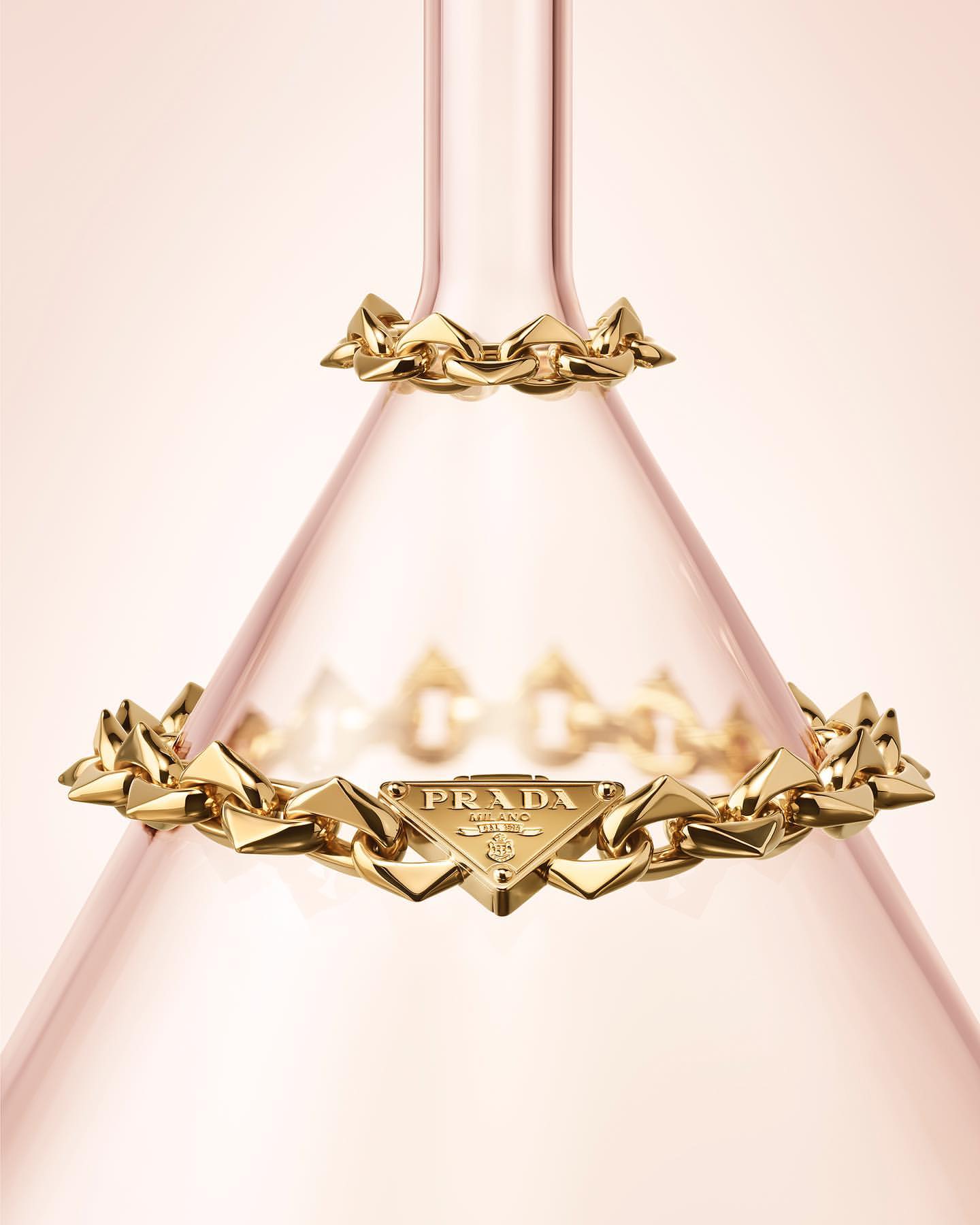 Gold chain bracelets with Prada logo on a light pink background. Fashion jewelry still life photography. Luxury goods advertising.