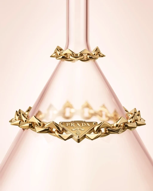 Gold chain bracelets with Prada logo on a light pink background. Fashion jewelry still life photography. Luxury goods advertising.