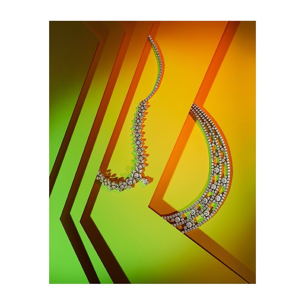Two diamond necklaces are displayed against a vibrant backdrop of yellow and green, casting sharp shadows for a striking jewelry still life.