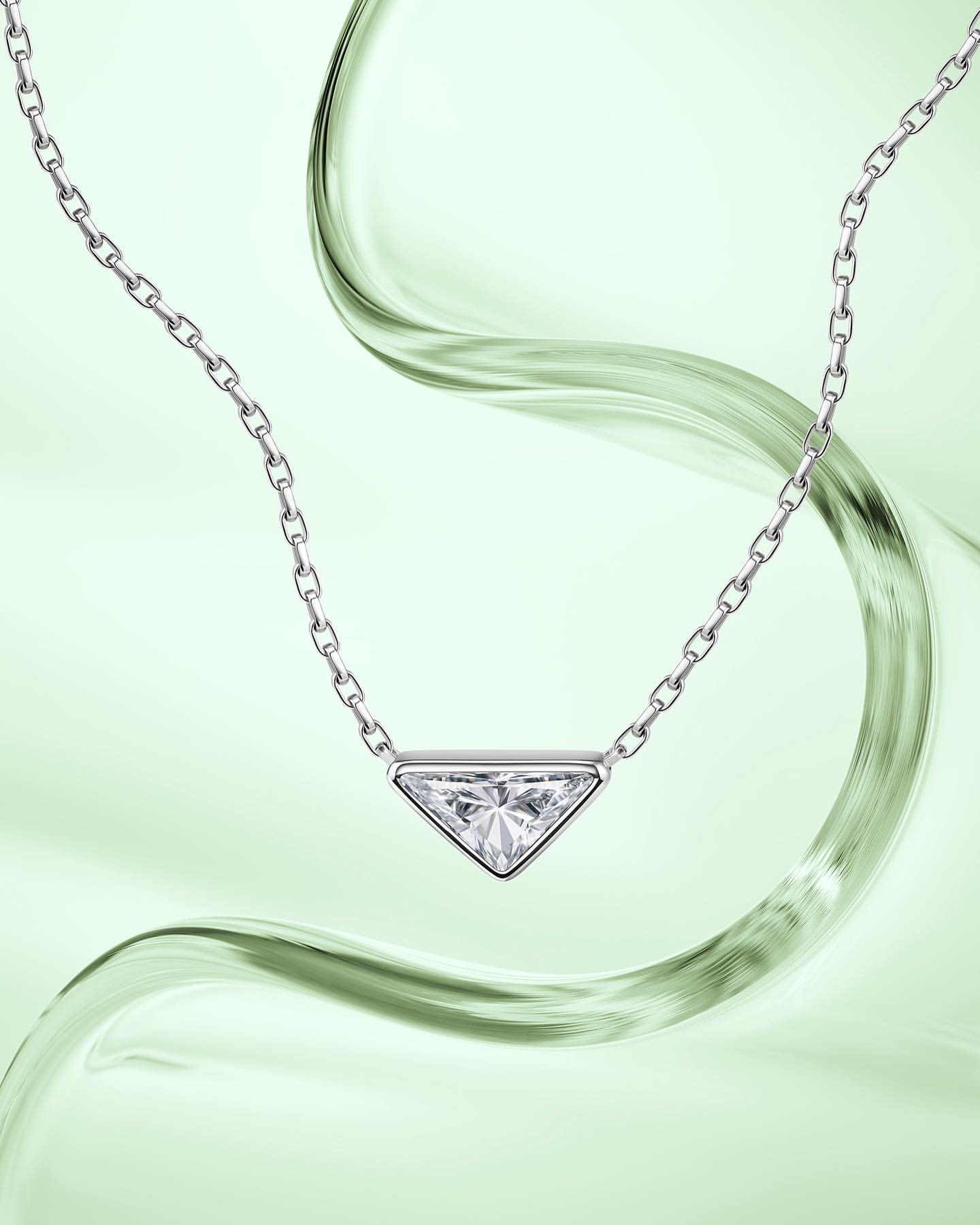Elegant jewelry shot: Silver chain necklace featuring a triangular pendant with a clear stone on a light green background with fluid motion.