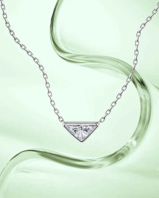 Elegant jewelry shot: Silver chain necklace featuring a triangular pendant with a clear stone on a light green background with fluid motion.