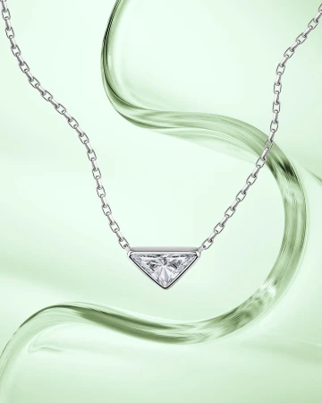 Elegant jewelry shot: Silver chain necklace featuring a triangular pendant with a clear stone on a light green background with fluid motion.