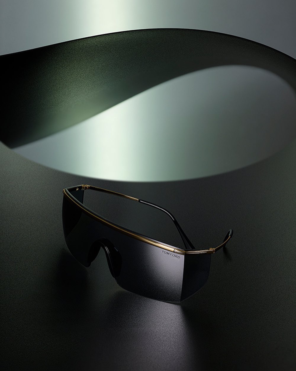 Studio shot of Tom Ford sunglasses on a dark surface, complemented by a curved grey background for a modern, sleek fashion aesthetic.