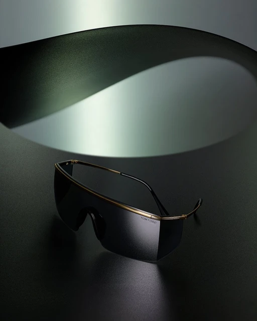Studio shot of Tom Ford sunglasses on a dark surface, complemented by a curved grey background for a modern, sleek fashion aesthetic.