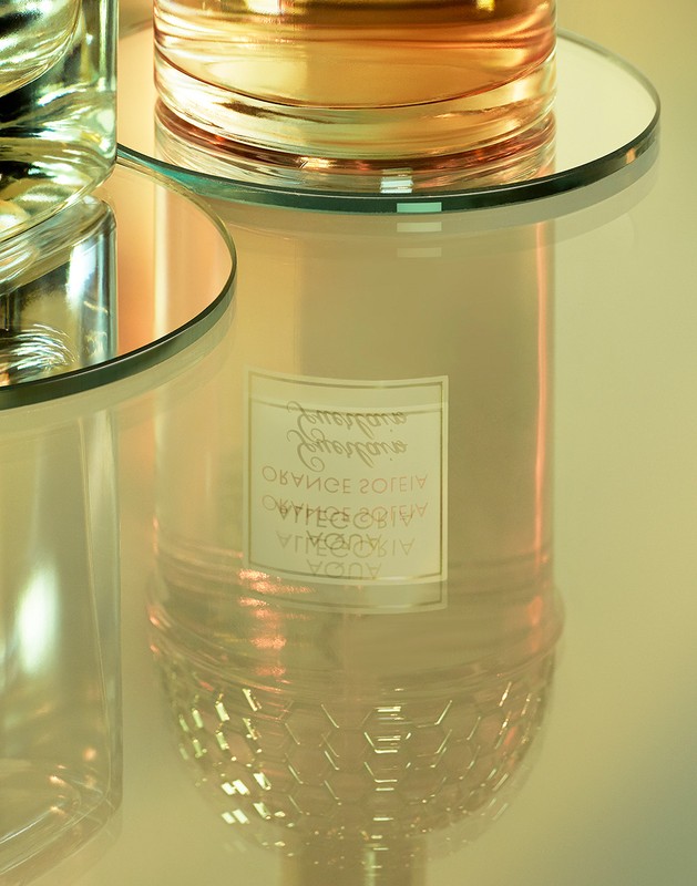 Close-up of two clear glass bottles filled with amber liquid on reflective surfaces, capturing a modern and minimalist aesthetic.