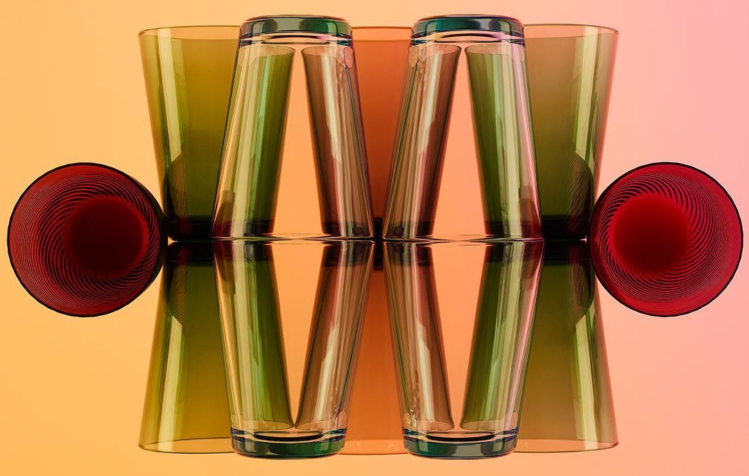 Artistic still life featuring clear and colored drinking glasses arranged on a reflective surface with a gradient background.
