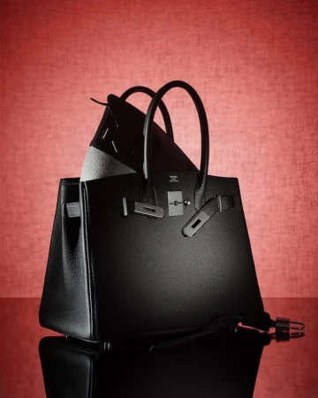Still life shot of two black leather handbags with silver hardware, set against a textured red background with a reflective surface.