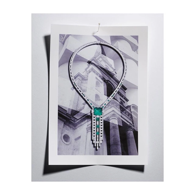 Elegant diamond and emerald necklace artfully displayed on a print featuring architectural details in a refined, indoor composition.