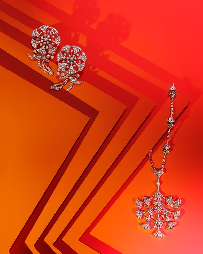 Floral-design diamond necklace and earrings on a colorful orange and red geometric background, shot for beauty and jewelry advertising.