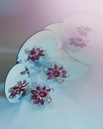 Close-up product photograph of ruby and diamond floral brooches reflected in multiple angled circular mirrors.