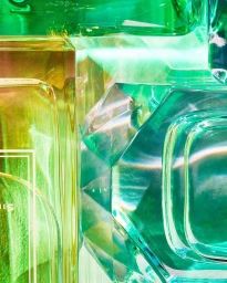 Close-up macro shot of translucent faceted green and yellow glass perfume bottles with vibrant refracted light refractions.